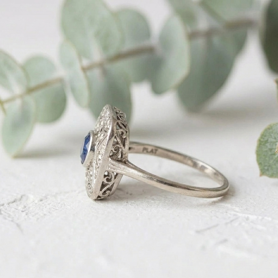 Art Deco Sapphire Diamond Ring featuring a 0.50 CT round cut deep blue natural sapphire in a square halo setting with round lab grown diamond accents and vintage inspired white metal detailing.