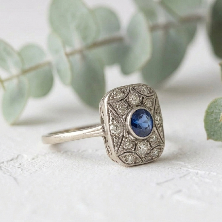 Art Deco Sapphire Diamond Ring featuring a 0.50 CT round cut deep blue natural sapphire in a square halo setting with round lab grown diamond accents and vintage inspired white metal detailing.