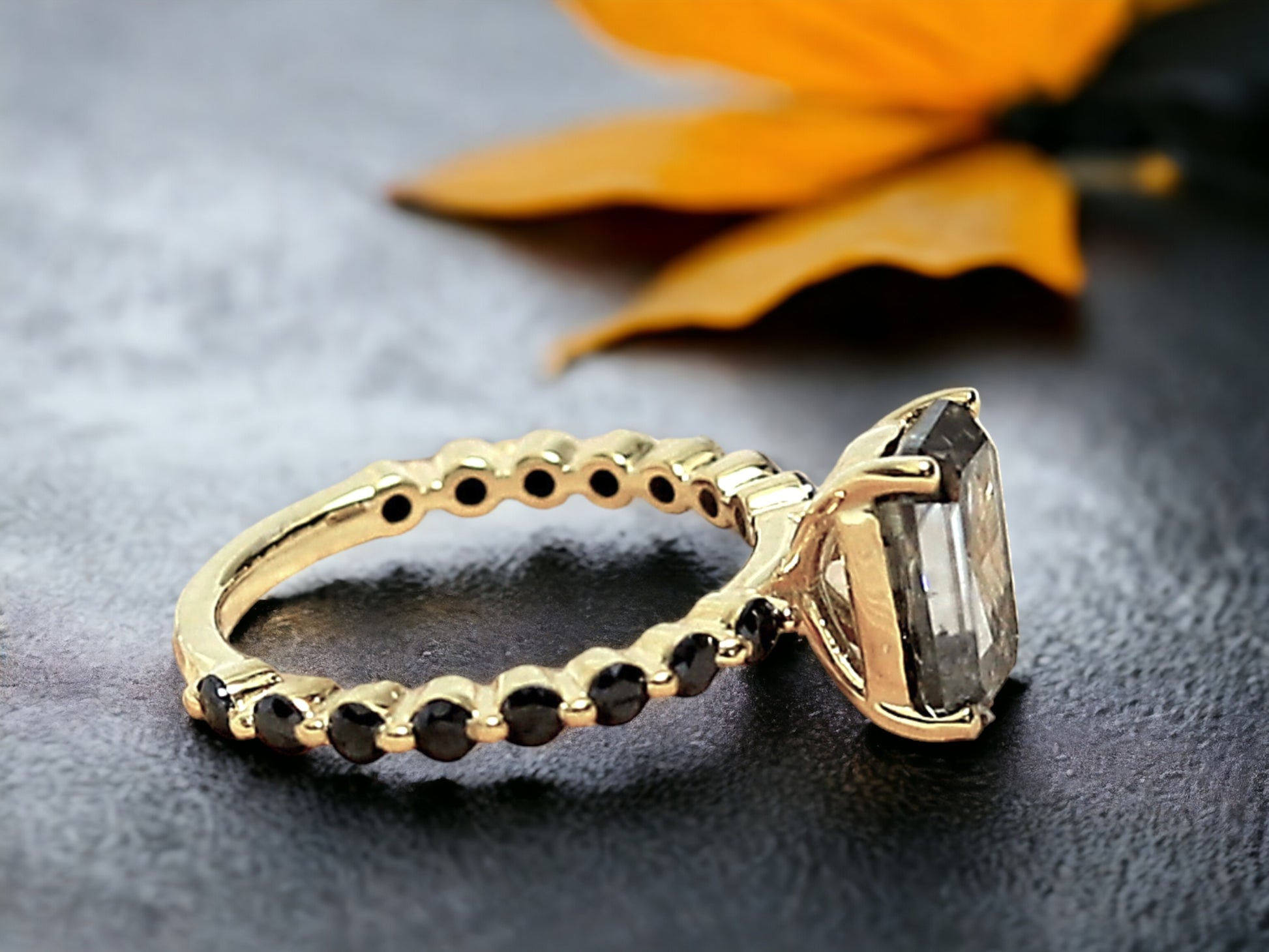 Emerald Cut Salt and Pepper Diamond Ring featuring a 2.58 CT natural salt and pepper diamond with speckled galaxy-like inclusions in a minimalist bezel setting, accented by 16 round brilliant diamonds in a straight 1.80 mm band for a modern geometric design.