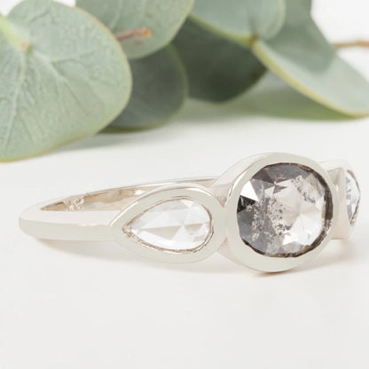 Oval cut salt and pepper diamond engagement ring featuring a 2.50 CT natural center stone with pear shaped side diamonds, set on a handcrafted knife edge band in a modern vintage fusion design.