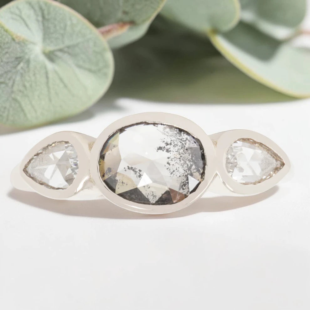 Oval cut salt and pepper diamond engagement ring featuring a 2.50 CT natural center stone with pear shaped side diamonds, set on a handcrafted knife edge band in a modern vintage fusion design.