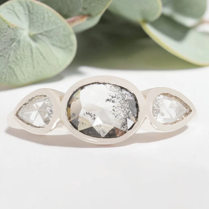 Oval cut salt and pepper diamond engagement ring featuring a 2.50 CT natural center stone with pear shaped side diamonds, set on a handcrafted knife edge band in a modern vintage fusion design.