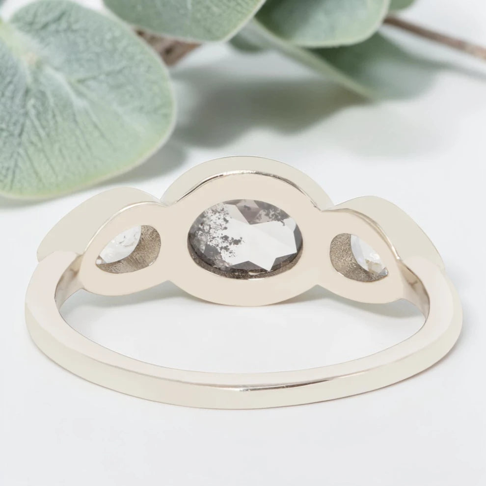 Oval cut salt and pepper diamond engagement ring featuring a 2.50 CT natural center stone with pear shaped side diamonds, set on a handcrafted knife edge band in a modern vintage fusion design.