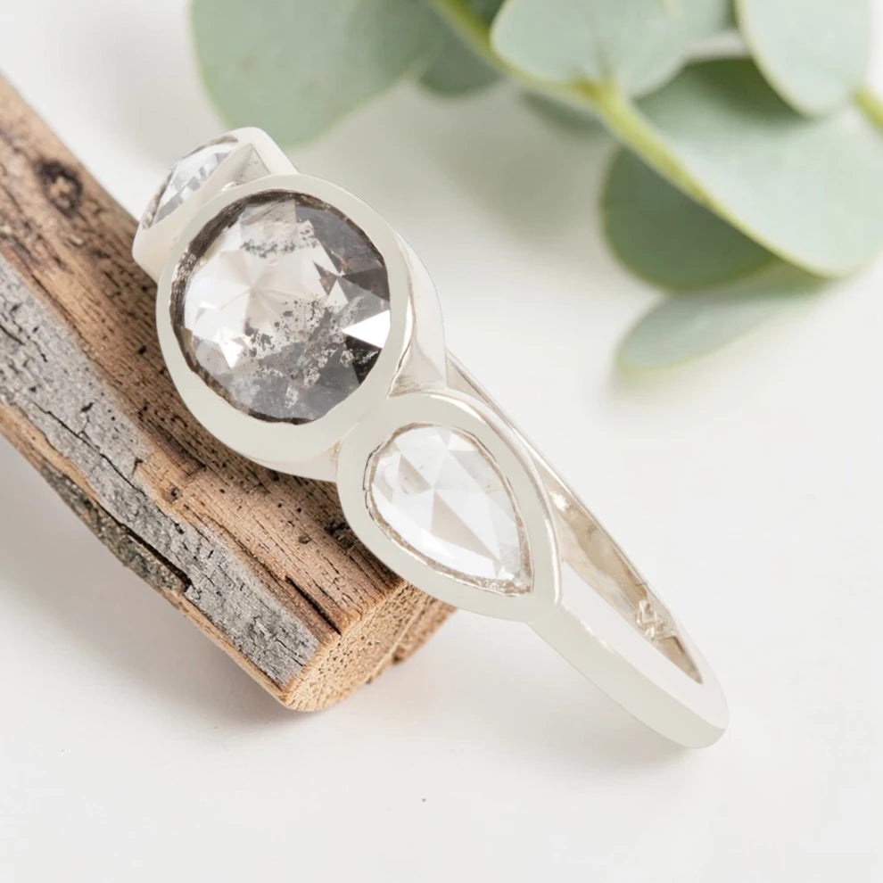 Oval cut salt and pepper diamond engagement ring featuring a 2.50 CT natural center stone with pear shaped side diamonds, set on a handcrafted knife edge band in a modern vintage fusion design.