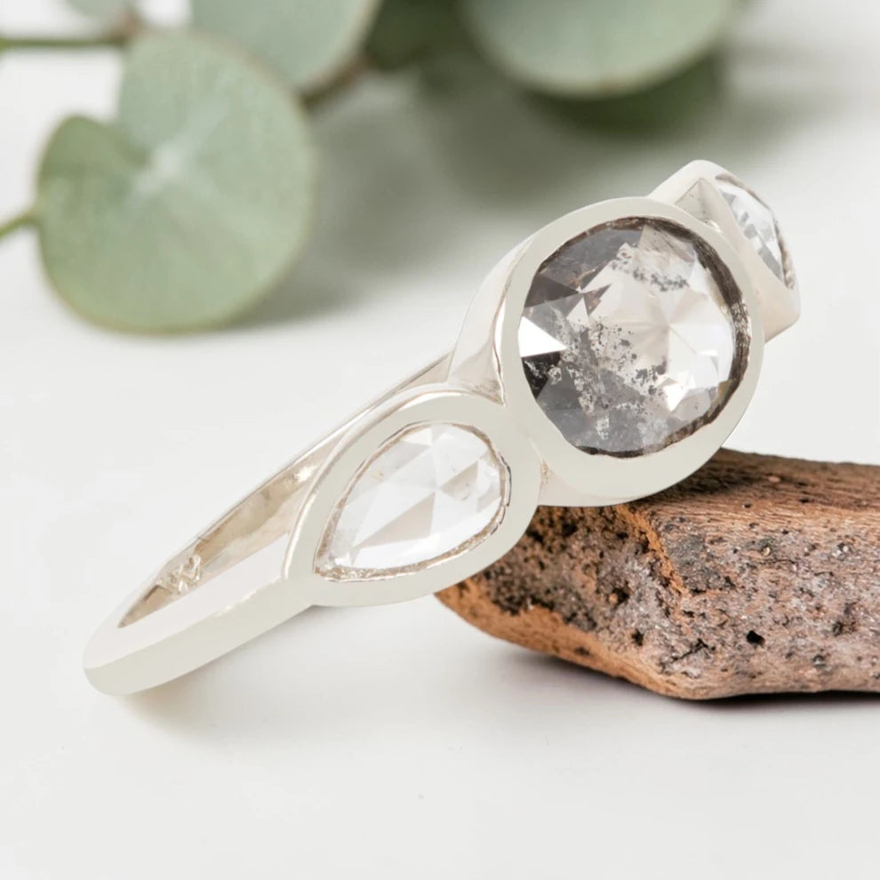 Oval cut salt and pepper diamond engagement ring featuring a 2.50 CT natural center stone with pear shaped side diamonds, set on a handcrafted knife edge band in a modern vintage fusion design.