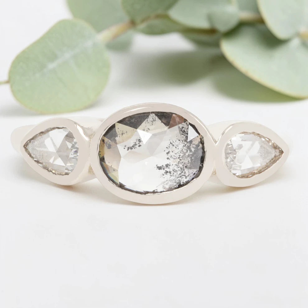 Oval cut salt and pepper diamond engagement ring featuring a 2.50 CT natural center stone with pear shaped side diamonds, set on a handcrafted knife edge band in a modern vintage fusion design.