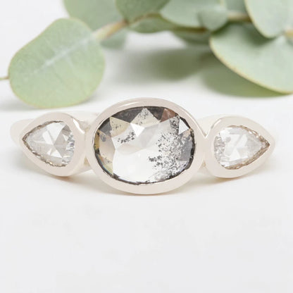 Oval cut salt and pepper diamond engagement ring featuring a 2.50 CT natural center stone with pear shaped side diamonds, set on a handcrafted knife edge band in a modern vintage fusion design.