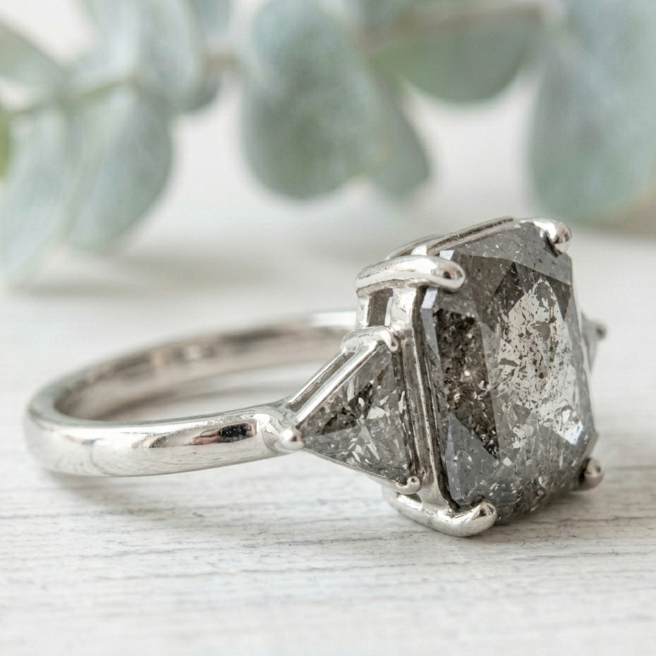 Rose Emerald Cut Salt and Pepper Diamond Ring featuring a 2.58 CT natural salt and pepper diamond with smoky galaxy-like inclusions, accented by triangle cut diamonds in a handcrafted, vintage-inspired, alternative engagement design with a straight 1.80 mm band.