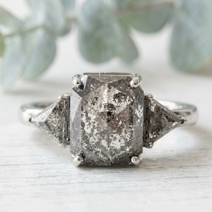 Rose Emerald Cut Salt and Pepper Diamond Ring featuring a 2.58 CT natural salt and pepper diamond with smoky galaxy-like inclusions, accented by triangle cut diamonds in a handcrafted, vintage-inspired, alternative engagement design with a straight 1.80 mm band.